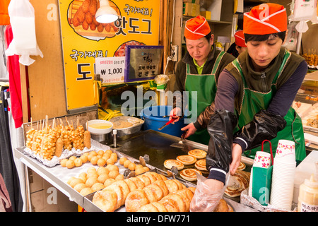 Bancarella vendendo hotdog, ciambelle e hotteok in al Mercato Namdaemun, Seoul, Corea (uomo sulla sinistra fa hotteok sulla sommità piana grill) Foto Stock