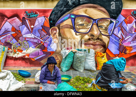 Street sellers in front of a wall covered by graffiti, Otavalo market, Imbabura Province, Ecuador Foto Stock