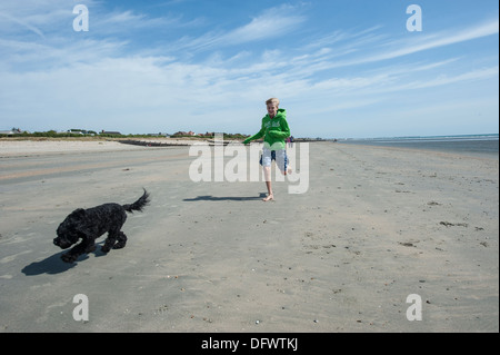 Un giovane ragazzo corre attraverso un inglese di spiaggia con il suo cane nero Foto Stock