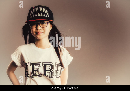 Una ragazza asiatica in un nerd t-shirt e un cappello da baseball con denti Foto Stock