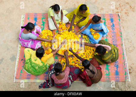 Rurale villaggio indiano le donne sedute intorno a un paniere di fiori di tagete fare ghirlande di fiori. Andhra Pradesh, India Foto Stock