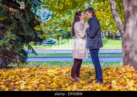 Coppia giovane in amore sul grande prato in autunno sotto grandi alberi di acero in autunno soleggiata giornata Foto Stock