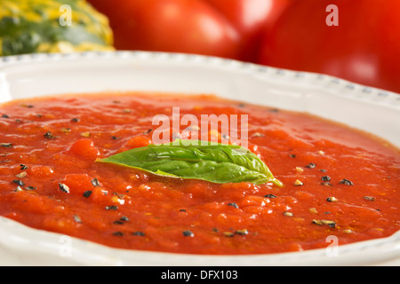 Primo piano di una casa fatta di zuppa di pomodoro con foglie di basilico e pomodori con squash zucche in background Foto Stock
