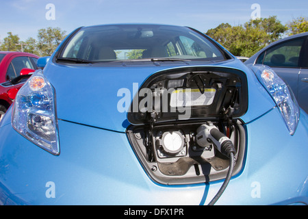 Blue plug-in auto elettrica con il connettore collegato a una stazione di carica per caricare la batteria in una società di parcheggio Foto Stock