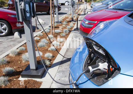 Plug-in di auto elettriche inserito in un VE stazione di carica per caricare le batterie in un luogo di lavoro parcheggio Foto Stock