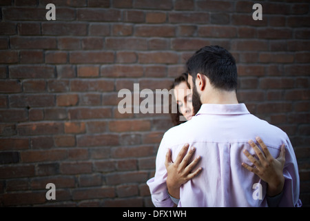 Vista posteriore del giovane uomo essendo abbracciato dalla sua ragazza Foto Stock