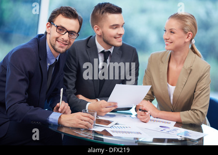 Imprenditore di successo guardando la fotocamera al lavoro mentre il suo partner discutere le idee sullo sfondo Foto Stock