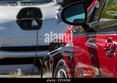 Red plug-in auto elettrica inserita in un VE stazione di carica per caricare le batterie in un luogo di lavoro parcheggio Foto Stock