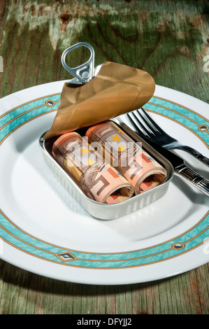 Una lattina può con denaro su una piastra con argenti, posto un vecchio tavolo in legno Foto Stock