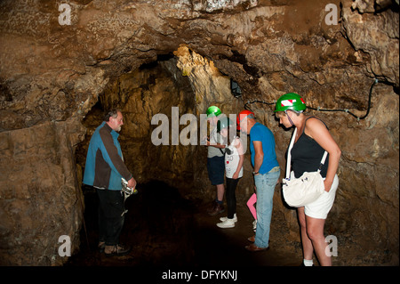 Gruppo di turisti ad esplorare Smoo Cave fiume sotterraneo Indossare copricapi rigidi Foto Stock