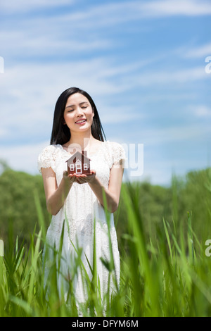 Felice giovane donna in possesso di un modello di casa sull'erba Foto Stock