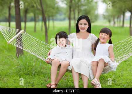 Felice giovane madre e bambini seduti in un amaca all'aperto Foto Stock