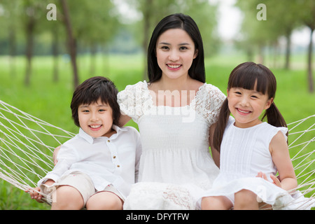 Felice giovane madre e bambini seduti in un amaca all'aperto Foto Stock
