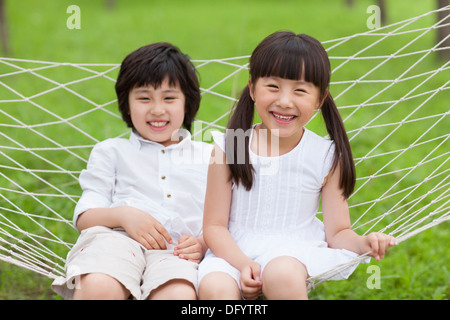 Emozionato i bambini seduti in un amaca all'aperto Foto Stock