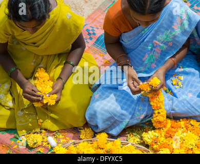 Rurale villaggio indiano le donne sedute intorno a un paniere di fiori di tagete fare ghirlande di fiori. Andhra Pradesh, India Foto Stock