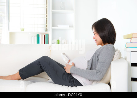 Bella donna incinta mettendo le cuffie sul suo ventre mentre giaceva su un letto di casa Foto Stock