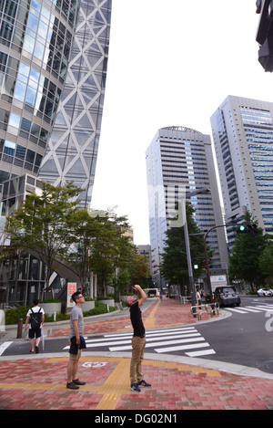 Grattacieli in stazione di Shinjuku Uscita Ovest area nel centro di Tokyo. Uomo che guarda verso l'alto di scattare una foto di un edificio alto Foto Stock