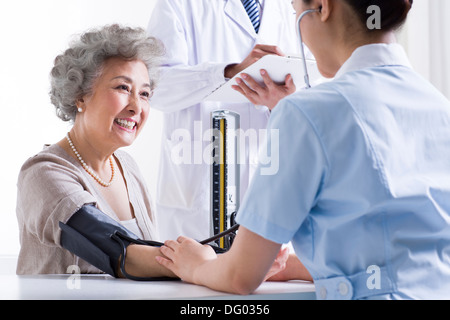 L'infermiera prendere senior donna della pressione del sangue Foto Stock