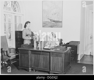 Questa fotografia mostra Rose Conway, la segretaria del presidente Harry S. Truman, alla sua scrivania nell'ufficio della Casa Bianca. Sta conversando con un individuo sconosciuto, catturando un momento della vita amministrativa quotidiana nell'amministrazione Truman. Foto Stock