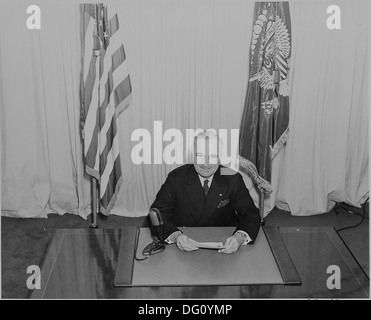 Il presidente Harry Truman seduti ad una scrivania, prima di un microfono, annunciando la fine della II Guerra Mondiale in Europa. 199075 Foto Stock