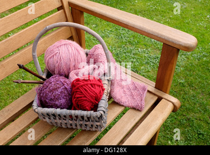 Cestello di artigianato di lavorazione a maglia a motivi geometrici, palline di lana e aghi di legno su una panchina da giardino Foto Stock