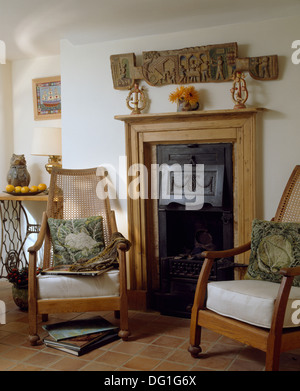 Scultura in legno sulla parete sopra il pino camino in bianco cottage soggiorno con canna sedie a schienale cava e pavimento piastrellato Foto Stock