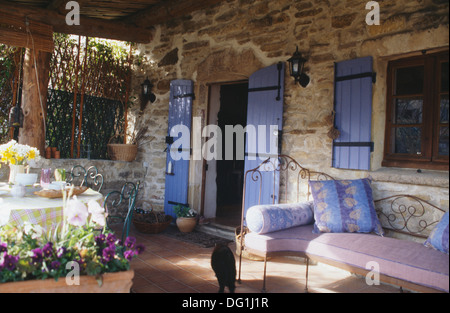 Persiane blu su porte e finestre che si affacciano sulla veranda con cuscini rosa sul ferro battuto letto da giorno Foto Stock