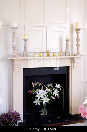 Portacandele su marmo mantelpiece al di sopra di un vaso di gigli bianchi nel camino in bianco pannellata soggiorno Foto Stock