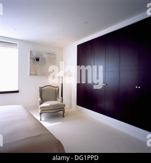 Grigio in stile Regency poltrona accanto al guardaroba a muro con legno scuro porte in città moderna camera da letto con tappeto bianco Foto Stock