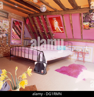 Specchio esposta su un muro di mattoni accanto al grande letto di metallo in datato rosa camera mansardata con soffitto di colore giallo e rosa con fodera in pelliccia sintetica rug Foto Stock