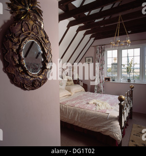 Ornati in uno specchio antico e letto in ottone nel paese mansarda camera da letto con travi esposte nel soffitto apex Foto Stock
