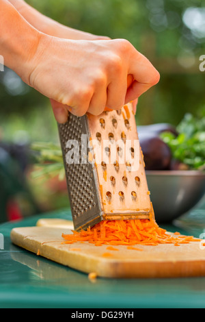 Donna mani grattugiare la carota su una griglia metallica di close-up Foto Stock