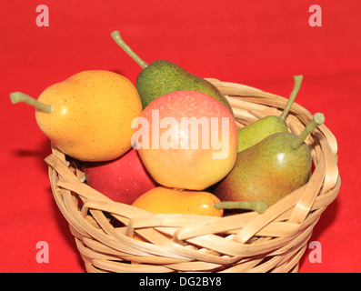 Frutta, pere e mele in un tan cesto su uno sfondo rosso Foto Stock