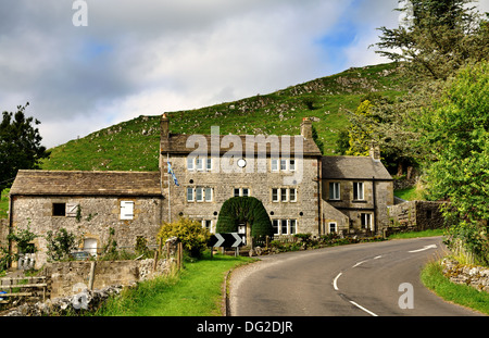 Un tradizionale cottage in pietra insieme contro una collina erbosa, da una piegatura della strada nel Derbyshire, Inghilterra Foto Stock