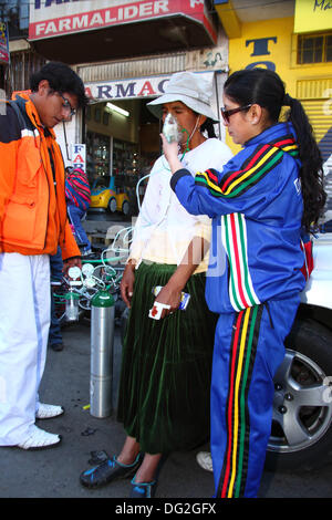 El alto, Bolivia. 12 ottobre 2013. A un concorrente viene dato ossigeno per aiutare a recuperare dagli effetti dello sforzo ad alta quota dopo aver completato una corsa ciclistica Cholitas per donne indigene Aymara. La gara si svolge ad un'altitudine di poco più di 4.000 m lungo le strade principali della città di El alto (sopra la Paz) per il Womens Day boliviano, che si è svolto ieri venerdì 11 ottobre. Crediti: James Brunker / Alamy Live News Foto Stock
