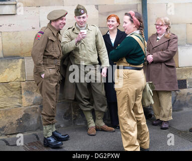 Un gruppo di amici in chat in Park Street Pickering North Yorkshire England Regno Unito nel periodo abiti per il tempo di guerra e 1940's week-end 2013. Un uomo isdressed come British Royal Artillery gunner e gli altri come un paracadutista americano. Una Donna vestita come un esercito di terra ragazza gli altri come i civili. Foto Stock