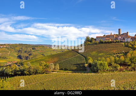 Piccola tipica città italiana sulla collina sopra i vigneti autunnali sotto il bellissimo cielo in Piemonte, Italia settentrionale. Foto Stock