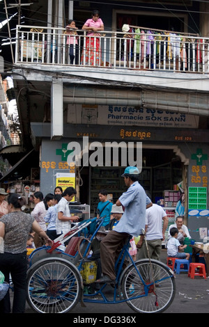 Un driver cyclo è in cerca di clienti mentre pedala su una strada trafficata riempita con gli acquirenti in Phnom Penh Cambogia. Foto Stock