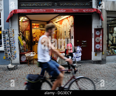 Un ciclista il passaggio di un laccio shop in Bruges Belgio Foto Stock