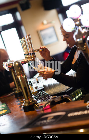 Una giovane donna femmina lavoratore barra di colata tirando una pinta di birra in un pub inn REGNO UNITO Foto Stock