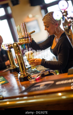 Una giovane donna femmina bar barista lavoratore versando tirando una pinta di birra chiara in un pub inn REGNO UNITO Foto Stock