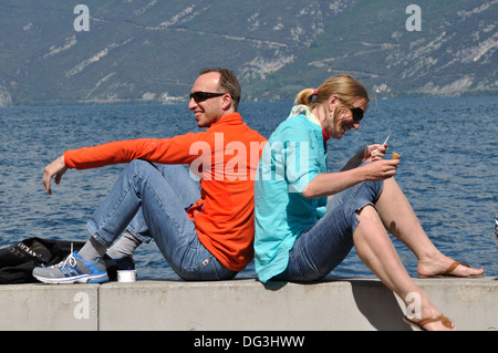 Sorridente coppia giovane sat di schiena su una parete in riva al lago a Limone sul Garda, Italia. Foto Stock