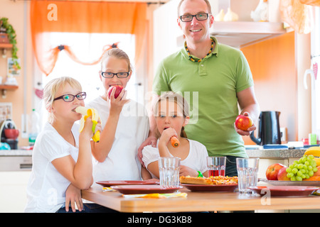 Famiglia, padre e figli o figlie con gli amici in cucina a tavola a mangiare frutti sani Foto Stock