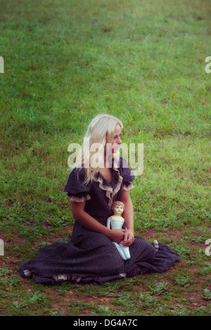 Una donna in un romantico abito con un vecchio doll su un prato Foto Stock