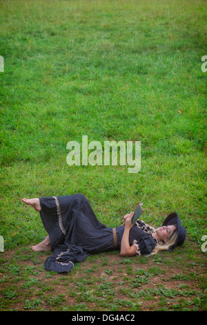 Una donna in un romantico abito è sdraiato su un prato, la lettura di un libro Foto Stock