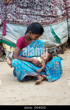 Giovani di casta inferiore ragazza indiana con il suo bambino seduto fuori il suo bender / tenda / rifugio. Andhra Pradesh, India Foto Stock