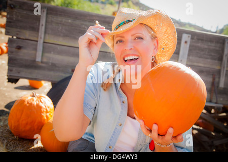 Bella Donna bionda Rancher indossando il cappello da cowboy detiene una zucca in un rustico di impostazione per il paese. Foto Stock