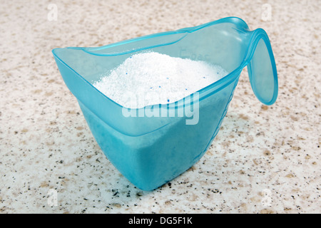 Detergente per lavanderia o detersivo in polvere in un blu coppa di misurazione su un bancone cucina top Foto Stock