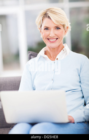 Sorridente donna senior utilizzando portatile a casa Foto Stock