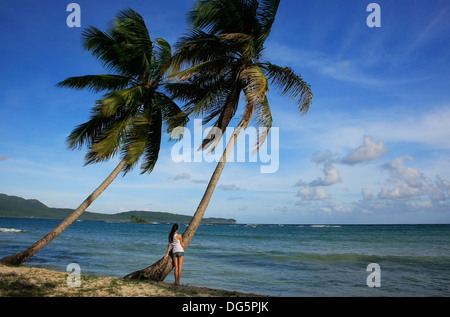 Giovane donna in piedi da palme, Las Galeras beach, penisola di Samana, Repubblica Dominicana Foto Stock